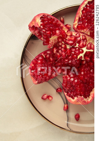 Half-cut pomegranate with seeds in plate on light background. Top view Half-cut pomegranate with seeds in plate on light background. Top view 126242785