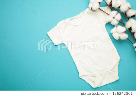 White baby short sleeve bodysuit with cotton flower on blue background. Top view 126242801
