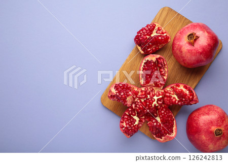 A whole pomegranate and a half-cut pomegranate with seeds on purple background. Top view A whole pomegranate and a half-cut pomegranate with seeds on purple background. Top view 126242813