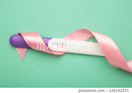The pregnancy test with two stripes with pink ribbon on mint background. Health care concept. Top view 126242855