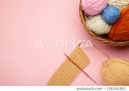 Balls of yarn in basket with knitting needles on pink background. Space for text 126242861