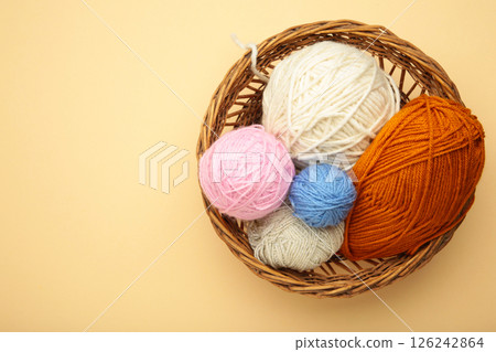 Balls of yarn in basket with knitting needles on beige background. Space for text 126242864