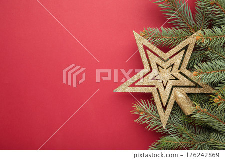Christmas frame made of fir branches, golden decorative star on red background. Space for text 126242869
