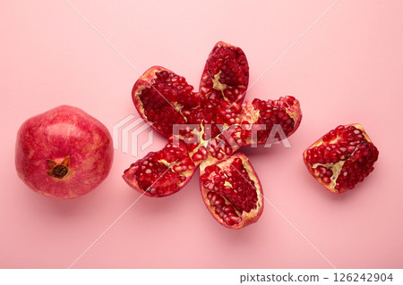 A whole pomegranate and a half-cut pomegranate with seeds on pink background. Top view 126242904