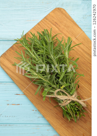 Fresh rosemary bunch on cutting board on blue wooden background Fresh rosemary bunch on cutting board on blue wooden background 126242970