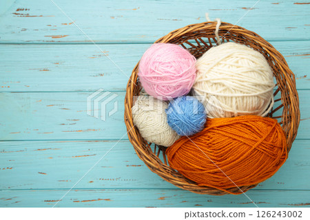 Balls of yarn in basket with knitting needles on blue wooden background. Space for text Balls of yarn in basket with knitting needles on blue wooden background. Space for text 126243002