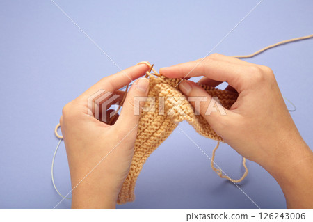 Women's hands knitting. Beige knitting yarns on violet background. 126243006