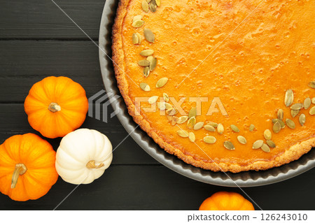 Delicious pumpkin pie with mini pumpkins on black wooden background. Thanksgiving day. Top view Delicious pumpkin pie with mini pumpkins on black wooden background. Thanksgiving day. Top view 126243010