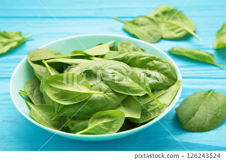 Spinach leaves with water drops in mint bowl on blue wooden background. Raw organic spinach greens. Vertical photo Spinach leaves with water drops in mint bowl on blue wooden background. Raw organic spinach greens. Vertical photo 126243524