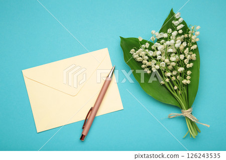 Invitation in a craft envelope with a spring bouquet of lilies of the valley on blue background. 126243535