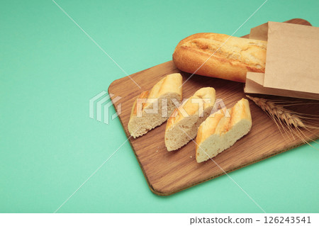 Baguette whole and cut into pieces on cutting board on mint background Baguette whole and cut into pieces on cutting board on mint background 126243541