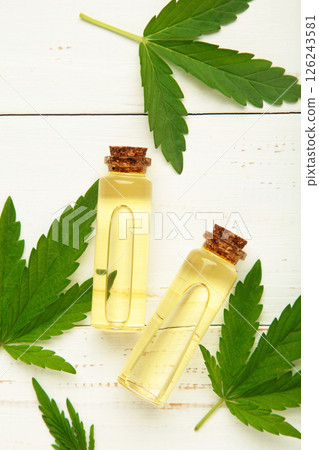 Little bottle with hemp oil and leaf on white wooden background. Vertical photo 126243581