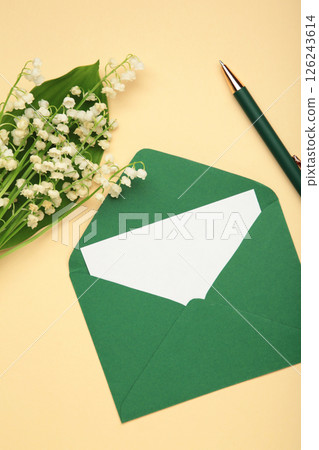 Invitation in a craft envelope with a spring bouquet of lilies of the valley on beige background. Vertical photo Invitation in a craft envelope with a spring bouquet of lilies of the valley on beige background. Vertical photo 126243614