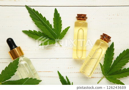 Little bottle with hemp oil and leaf on white wooden background. Little bottle with hemp oil and leaf on white wooden background. 126243689