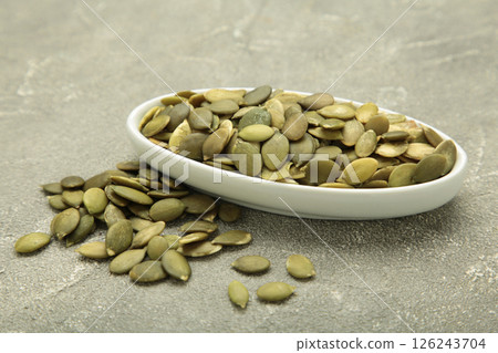 Pumpkin seeds in white bowl on grey concrete background, top view 126243704