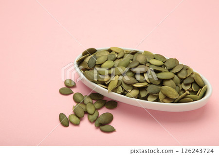 Pumpkin seeds in white plate on pink background. 126243724