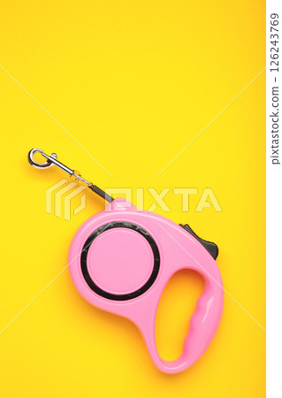 Pink plastic durable and ergonomic leash roulette for pets on yellow background. Convenient mechanical device for keeping and controlling dog in street. 126243769