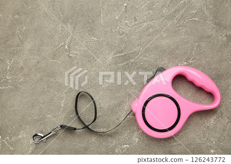 Pink plastic durable and ergonomic leash roulette for pets on grey concrete background. Convenient mechanical device for keeping and controlling dog in street. 126243772