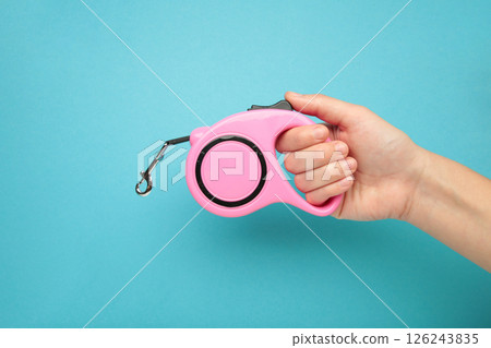 A hand holding a retractable dog leash on blue background. 126243835