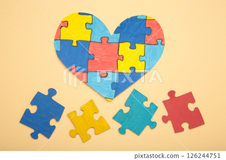 Colorful puzzle heart on beige background. Multi-colored heart as a symbol of World Autism Awareness Day. Top view Colorful puzzle heart on beige background. Multi-colored heart as a symbol of World Autism Awareness Day. Top view 126244751