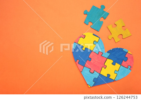 Colorful puzzle heart on orange background. Multi-colored heart as a symbol of World Autism Awareness Day. Top view 126244753