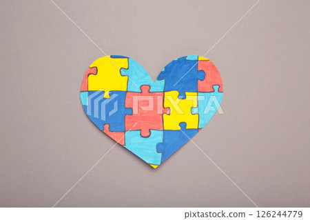 Colorful puzzle heart on grey background. Multi-colored heart as a symbol of World Autism Awareness Day. Top view Colorful puzzle heart on grey background. Multi-colored heart as a symbol of World Autism Awareness Day. Top view 126244779