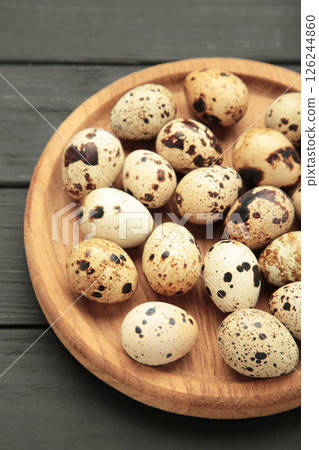 Quail eggs in wooden plate on black wooden background. Vertical photo. Quail eggs in wooden plate on black wooden background. Vertical photo. 126244860