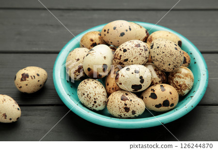 Quail eggs in blue bowl on black wooden background. Quail eggs in blue bowl on black wooden background. 126244870