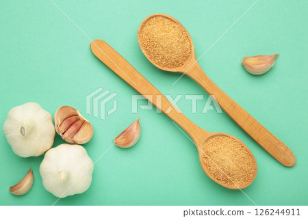 Fresh garlic and garlic powder in spoon on mint background. Using spices for meals. Top view 126244911