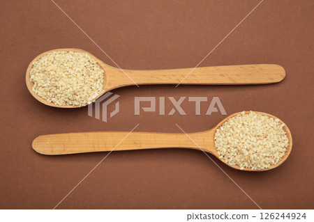 Organic white sesame seeds on wooden spoon on brown background. Organic white sesame seeds on wooden spoon on brown background. 126244924