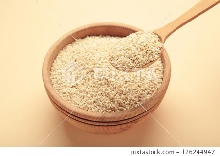 Raw sesame seeds in wooden bowl and spoon on beige background. Raw sesame seeds in wooden bowl and spoon on beige background. 126244947