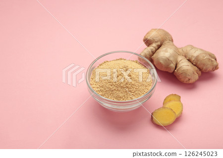 Dried ginger powder on bowl and fresh ginger root on pink background. Top view 126245023