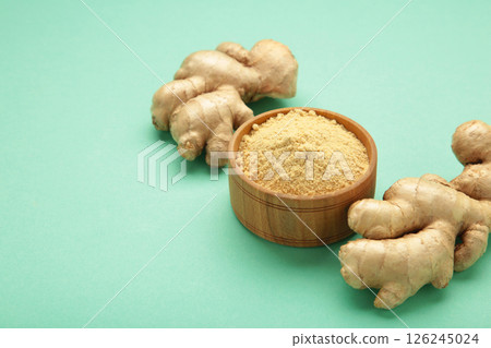 Wooden spoon with dried ginger powder and fresh ginger root on mint background. Top view 126245024