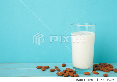 Fresh almond milk in glass and almonds on blue background. Healthy vegan plant based alternative milk replacer. 126245026