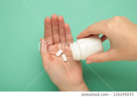 Woman holding pill and blank white plastic tube on mint background. Woman holding pill and blank white plastic tube on mint background. 126245035