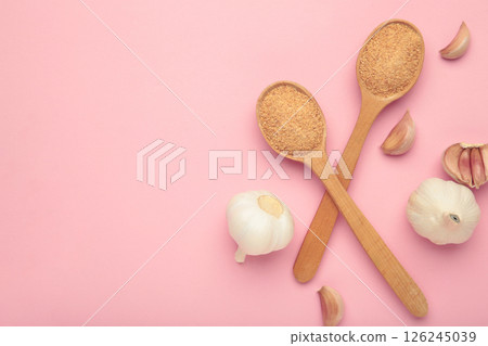 Fresh garlic and garlic powder in spoon on pink background. Using spices for meals. Top view Fresh garlic and garlic powder in spoon on pink background. Using spices for meals. Top view 126245039