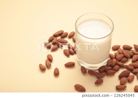 Fresh almond milk in glass and almonds on beige background. Healthy vegan plant based alternative milk replacer. 126245045
