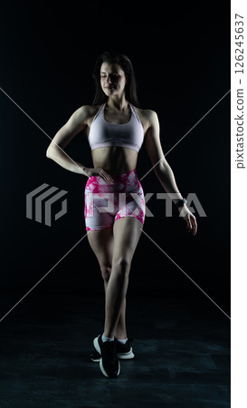Young beautiful fitness woman on a black background. Fitness girl, female bodybuilder on a dark background Young beautiful fitness woman on a black background. Fitness girl, female bodybuilder on a dark background 126245637