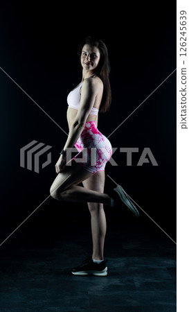 Young beautiful fitness woman on a black background. Fitness girl, female bodybuilder on a dark background Young beautiful fitness woman on a black background. Fitness girl, female bodybuilder on a dark background 126245639