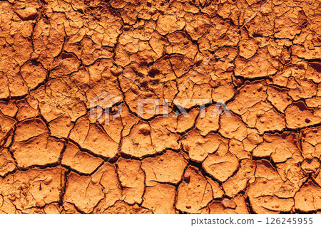Cracked Earth. An arid landscape with cracked, dry earth patterns in a warm orange hue Cracked Earth. An arid landscape with cracked, dry earth patterns in a warm orange hue 126245955