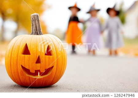 Halloween pumpkin sitting on street with children walking in background 126247946