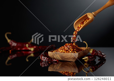 Dry red chili peppers and crushed chili flakes on a black reflective background. 126248011