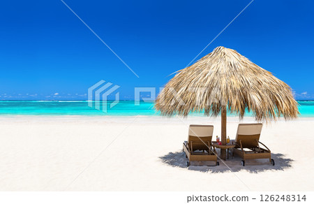 Beach chairs with umbrella and beautiful white sand beach in Punta Cana, Dominican Republic. Panorama of tropical beach with turquoise water. Beach chairs with umbrella and beautiful white sand beach in Punta Cana, Dominican Republic. Panorama of tropical beach with turquoise water. 126248314