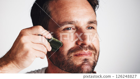 Skincare, gua sha and man in studio, cosmetics and dermatology on white background. Person, space and model with jade stone, self care and shine with wellness, beauty and facial treatment with glow Skincare, gua sha and man in studio, cosmetics and dermatology on white background. Person, space and model with jade stone, self care and shine with wellness, beauty and facial treatment with glow 126248827