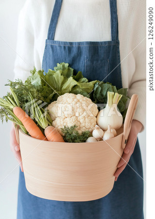 A woman wearing apron holding a basket full of fresh vegetables including carrots, leeks, and cauliflower, showcasing natural, healthy, and sustainable food origins. Vegetarian diet, eco food 126249090