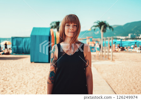 Portrait of a young smiling woman with a tattoo on her arm, looking at the camera. Sandy beach on the background. The concept of summer vacation Portrait of a young smiling woman with a tattoo on her arm, looking at the camera. Sandy beach on the background. The concept of summer vacation 126249974