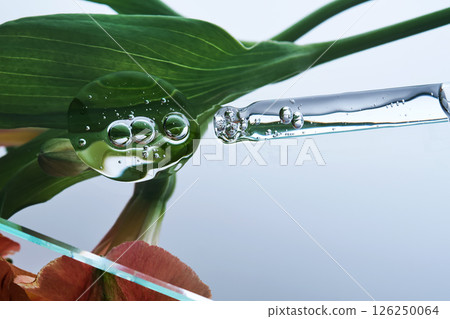 A pipette with a beautiful drop of serum on a background of lily flowers. A pipette with a beautiful drop of serum on a background of lily flowers. 126250064