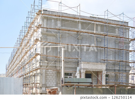 Large concrete building under construction with scaffolding and blue sky 126250114