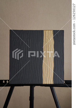 Textured black canvas painting with golden vertical line on easel in minimalist Textured black canvas painting with golden vertical line on easel in minimalist 126250127