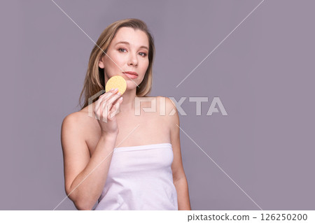 Caucasian young female holding facial sponge against gray background Caucasian young female holding facial sponge against gray background 126250200